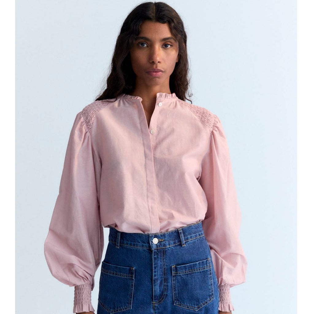 Person wearing a pink blouse with puffed sleeves and blue jeans on a light blue background