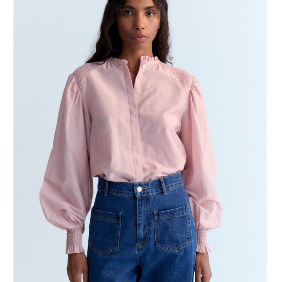 Person wearing a pink blouse with puffed sleeves and blue jeans on a light blue background