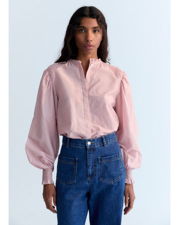 Person wearing a pink blouse with puffed sleeves and blue jeans on a light blue background